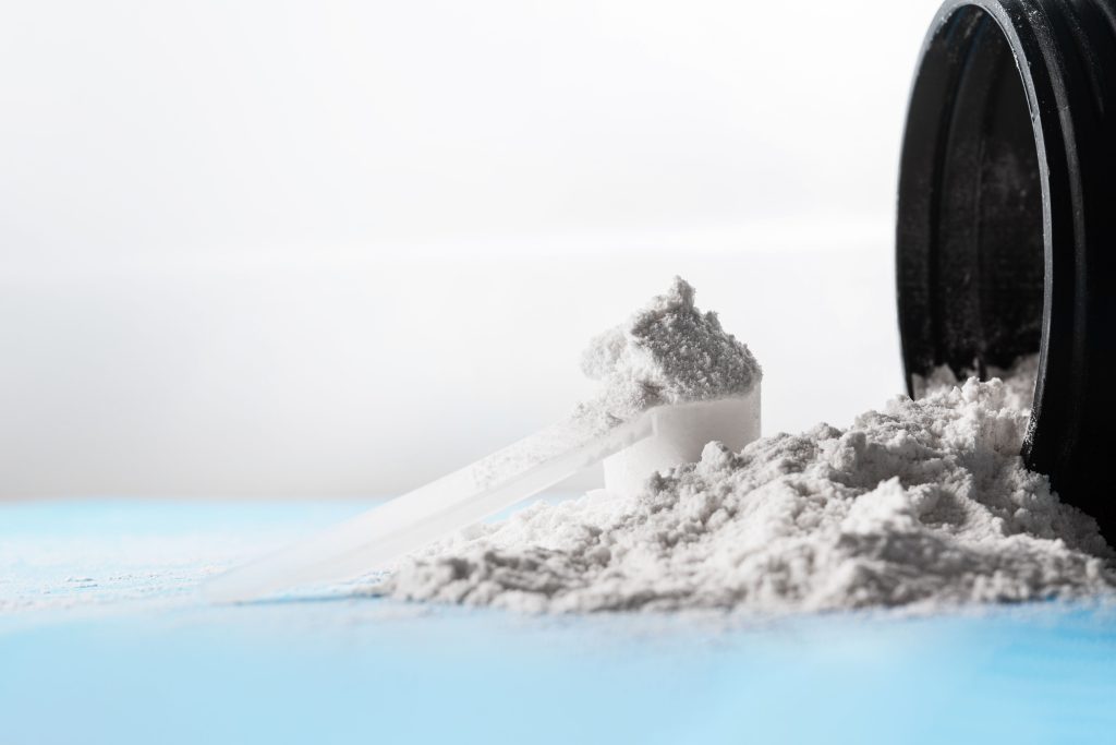 Closeup of a scoop of creatine powder on a scattered powder from the bottle on a blue surface