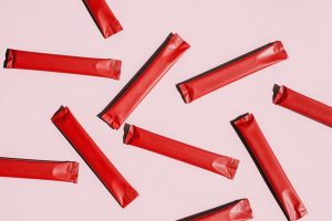 Several Red Stick Pack Sachets on Pink. Product Packaging Mockup for Nutrition Supplement Sample.