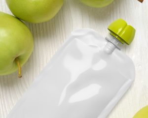 White empty plastic pouche for baby food, mock-up on wood table. 3d rendering.